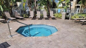 A swimming pool with a tiled deck, surrounded by lounge chairs and palm trees. - Beautiful 2-bedroom condo in a serene gated community with refreshing AC (Kissimmee)