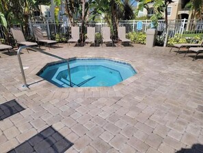 A swimming pool with a tiled deck, surrounded by lounge chairs and palm trees. - Beautiful 2-bedroom condo in a serene gated community with refreshing AC (Kissimmee)