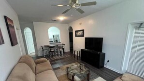 A living room with a ceiling fan, a TV, and a sofa. - Beautiful 2-bedroom condo in a serene gated community with refreshing AC (Kissimmee)