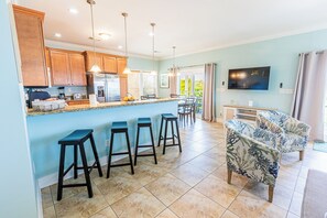 Une cuisine avec un coin bar, un espace repas avec un canapé et un téléviseur fixé au mur.