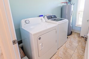 Ein Waschraum mit einer Frontlader-Waschmaschine und -trockner, einem Warmwasserbereiter und einem Fenster mit Jalousien.