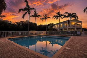 Ein Swimmingpool mit der Spiegelung von Palmen, umgeben von einer Ziegelterrasse und einem weißen Zaun.