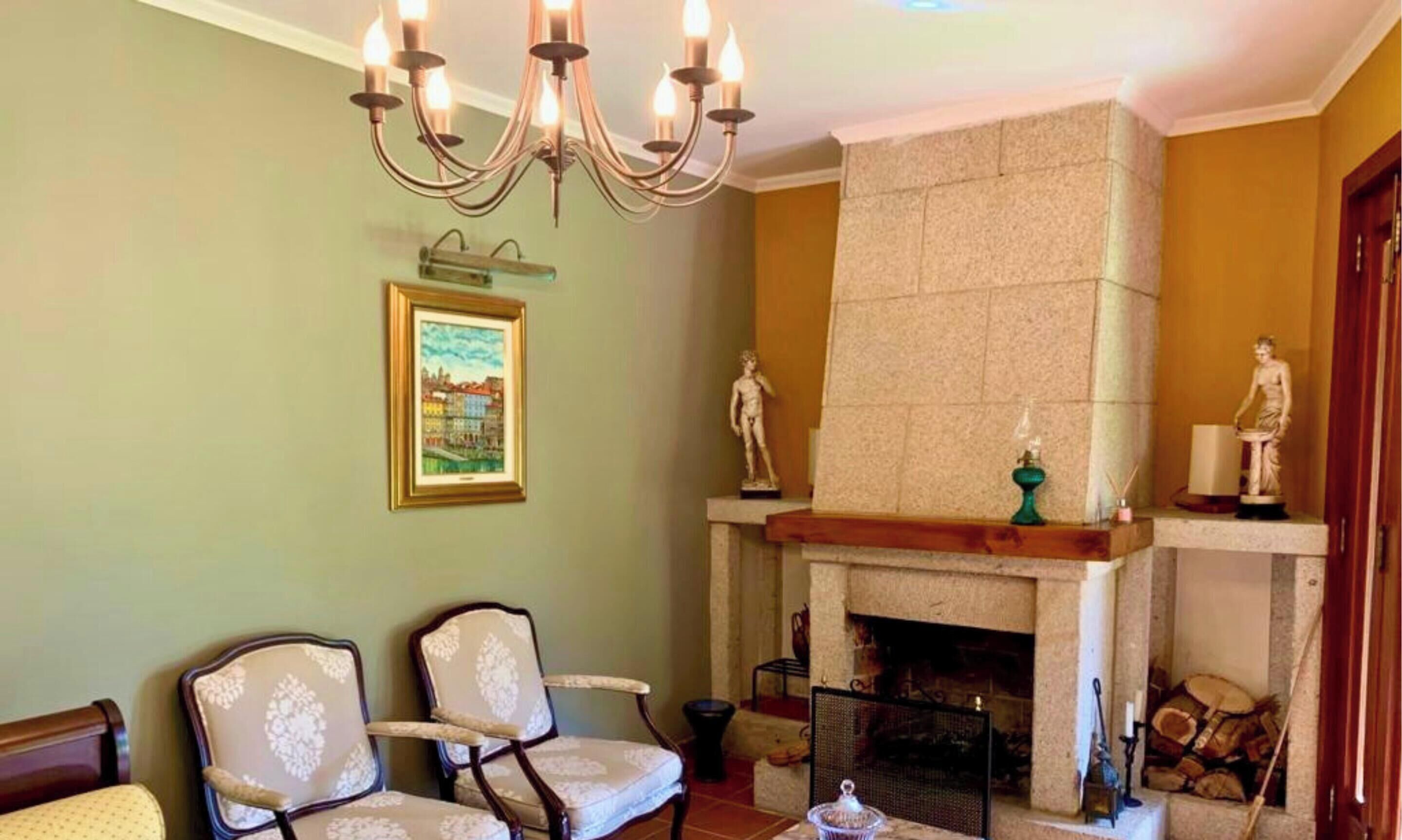 Une pièce avec une cheminée, deux fauteuils rembourrés, un tableau encadré et un lustre.