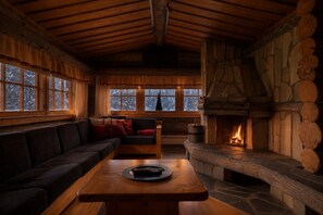 A cozy cabin interior with a stone fireplace, wooden furniture, and large windows. - Joikha Lapland Lodge by Aavalevi (Levi)
