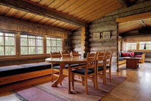 Ein rustikaler Innenraum einer Blockhütte mit einem runden Holzespeisetisch, Holzstühlen, einer Bank mit Kissen und einem Sofa.