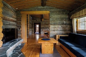 Ein rustikales Blockhaus-Interieur mit Kamin aus Stein, Holzmöbeln und einer gemütlichen Sitzecke.