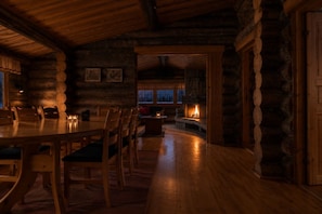 A log cabin interior with a dining area, fireplace, and a view of the outside.