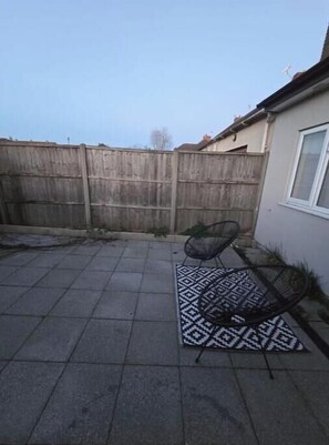 Eine Terrasse mit einem gemusterten Teppich, einem Stuhl und einem Holzzaun.