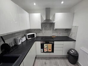 Eine kleine Küche mit weißen Schränken, einer schwarzen Arbeitsplatte, einem eingebauten Backofen und einer Mikrowelle.