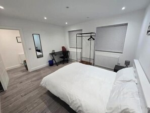 A bedroom with a large bed, a desk, a chair, a wardrobe, and a window with blinds. - Modern 1-Bed Apartment with Free Parking Near Heathrow Self Check-in (London)