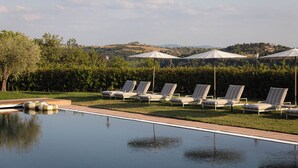 A poolside area with lounge chairs and umbrellas, a clear sky, and a hilly landscape in the background. - The Podere Wine Resort Chianti (Barberino Tavarnelle)