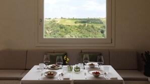 A dining table with plates of food, wine glasses, and cutlery, set against a backdrop of a scenic landscape through a window. - The Podere Wine Resort Chianti (Barberino Tavarnelle)