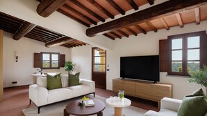 A spacious living room with a white sofa, a round coffee table, a flat-screen TV, and a wooden cabinet. - The Podere Wine Resort Chianti (Barberino Tavarnelle)