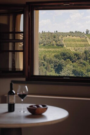 Una mesa con una botella de vino y una copa, un bol y una ventana con vistas a un viñedo.