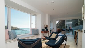 Ein modernes Interieur mit einer Sitzecke an einem großen Fenster mit Meerblick, einem Essbereich und einer Küche.