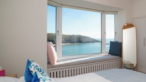 Ein Schlafzimmer mit großem Fenster, einem Bett, einer Sitzbank und einem Spiegel.