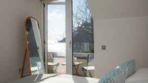 Ein Schlafzimmer mit einem Bett, einem Spiegel, einer Schiebetür zu einem Außenbereich und einem kleinen Tisch mit Stühlen.