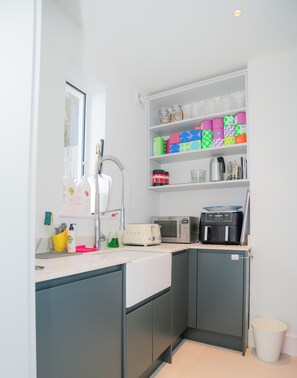 A compact kitchen with a microwave, toaster, and a shelf with colorful containers. - Luxury Estuary Views & Parking | Woodcot Cottage (Salcombe)