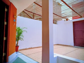 A room with a tiled floor, a potted plant, a wooden door, and a wall with a textured pattern.