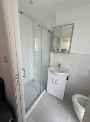 Ein Badezimmer mit Duschkabine aus Glas, einem weißen Waschbecken und einer Toilette.