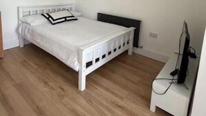 Una camera da letto con un letto bianco, un comodino, una televisione e un termosifone.