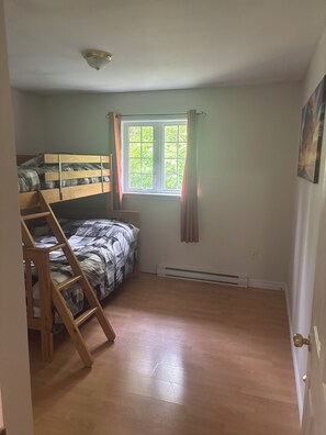 A room with a bunk bed, a ladder, a window with curtains, and a radiator.