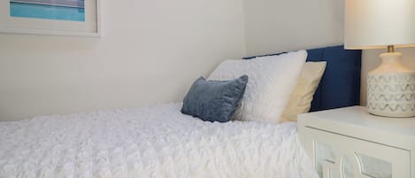 A neatly made bed with a textured white cover, a bedside table with a lamp, and a framed picture on the wall.