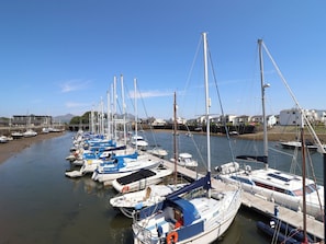 Un puerto deportivo con varias embarcaciones amarradas a lo largo del agua, un cielo despejado y edificios al fondo.