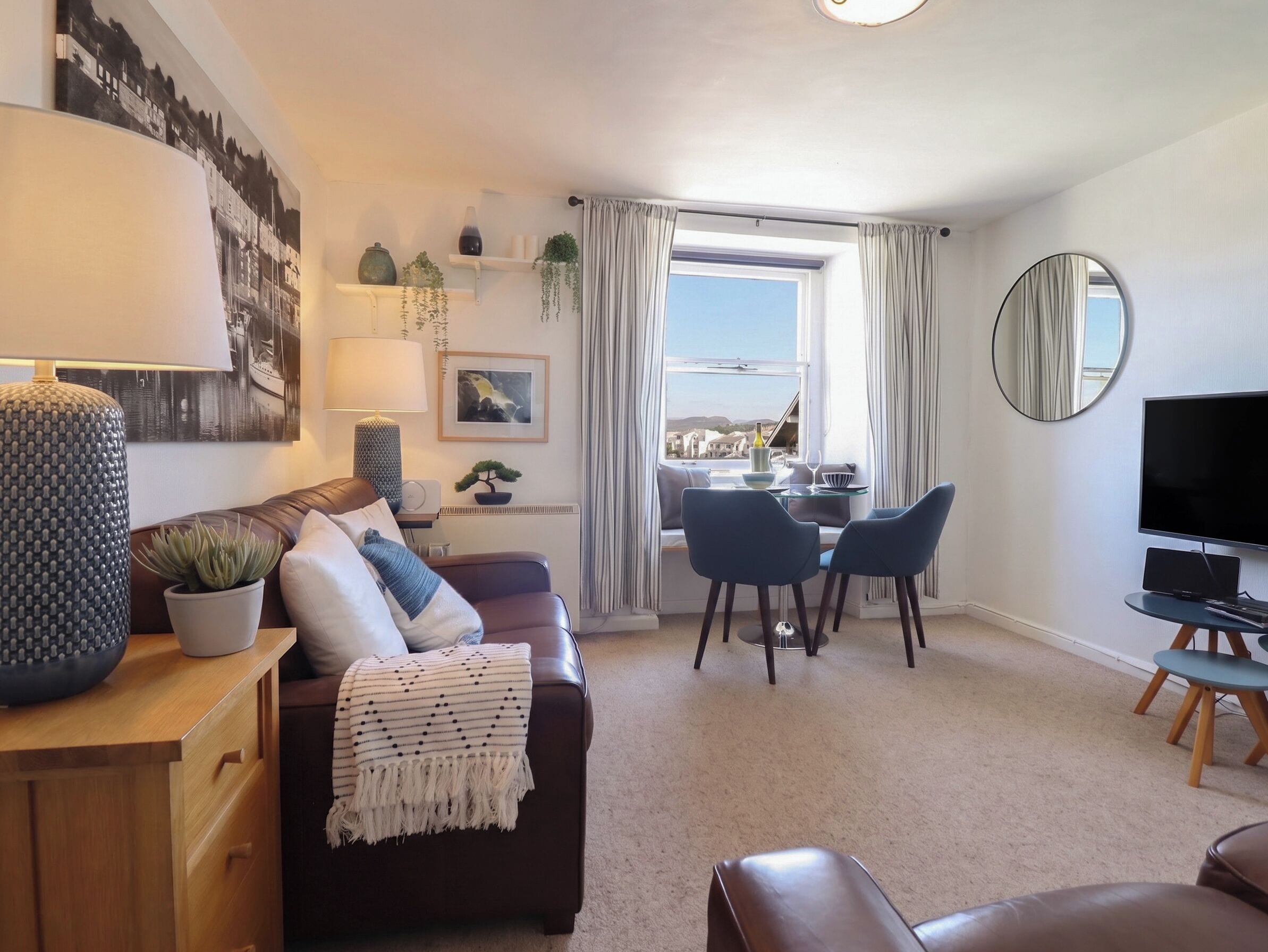 Een moderne woonkamer met een bank, een eethoek met stoelen, een televisie en een groot raam met gordijnen.