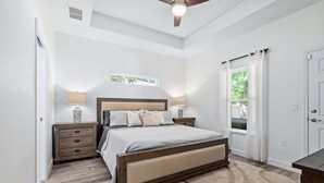 Un dormitorio con cama, mesitas de noche, una ventana con cortinas y un ventilador de techo.