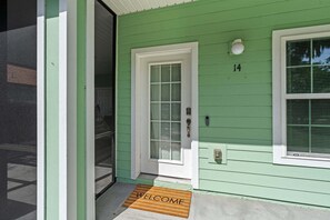 Una casa verde con puerta blanca, una ventana con persianas y felpudo.