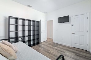 Un dormitorio con una cama, una estantería blanco y negro, una puerta blanca y un televisor montado.