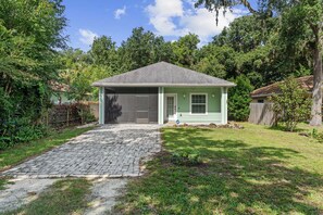 Une maison de plain-pied avec un garage, entourée d’une cour verdoyante et d’arbres.