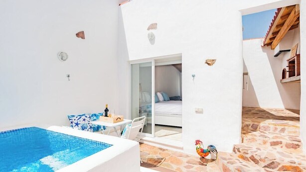 Uma área moderna da piscina exterior com porta de vidro para um quarto, chão em pedra e decoração com um galo.