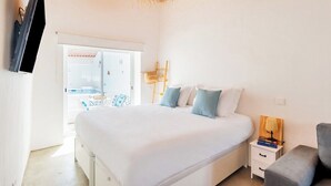 Quarto com cama, mesa de cabeceira, abajur e vista para área externa.