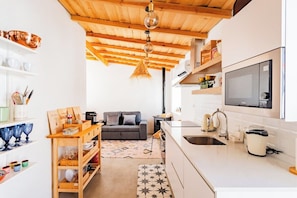 A compact kitchen with a wooden ceiling, a sofa, and a dining area with a table and chairs. - Alqueva Rustic Soul (Portel)