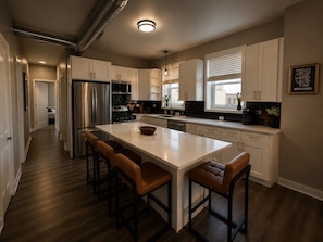 A modern kitchen with white cabinetry, a large island with stools, stainless steel appliances, and a view of the city.