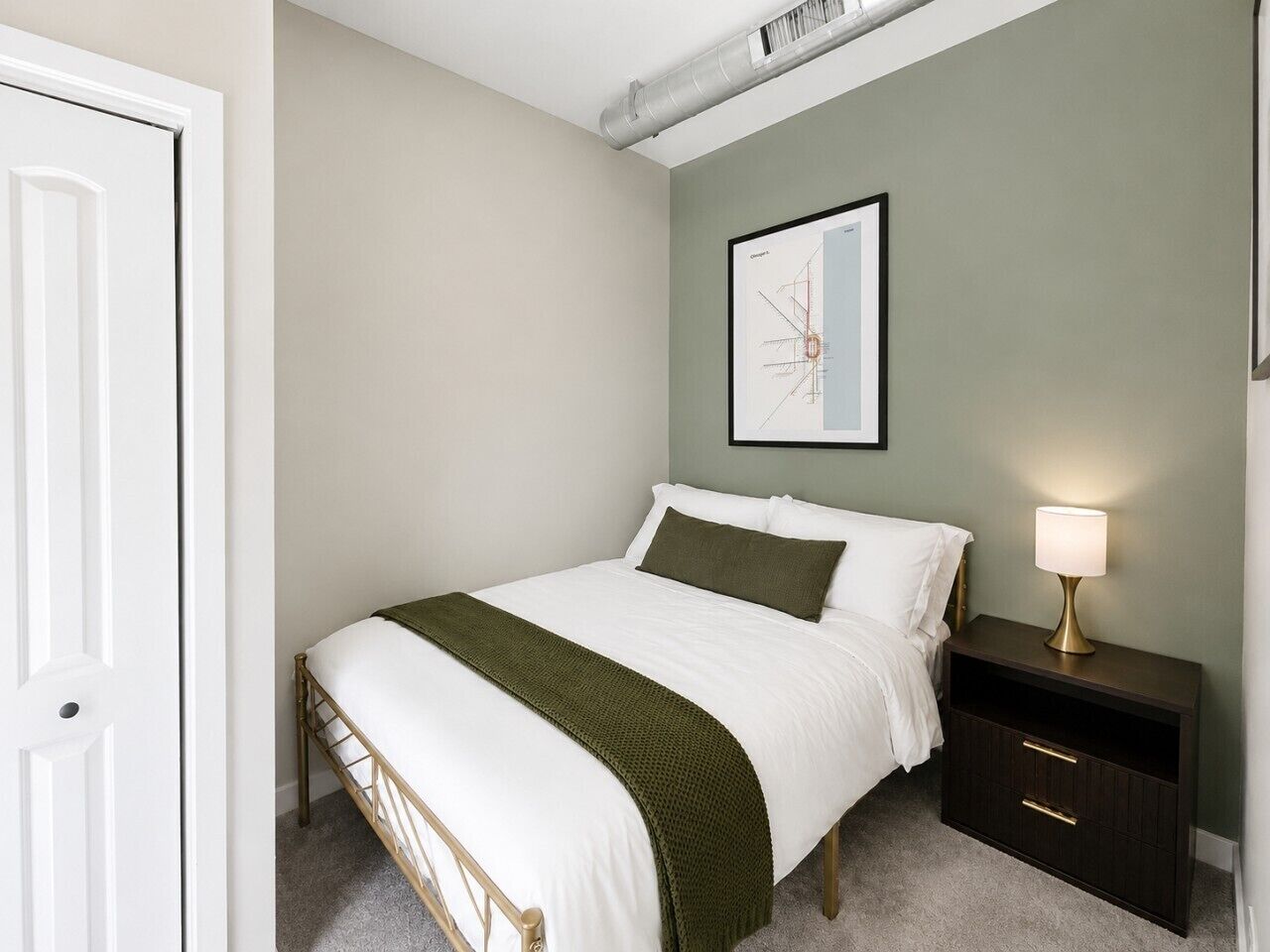 A bedroom with a bed, bedside table, lamp, and a framed picture on the wall.