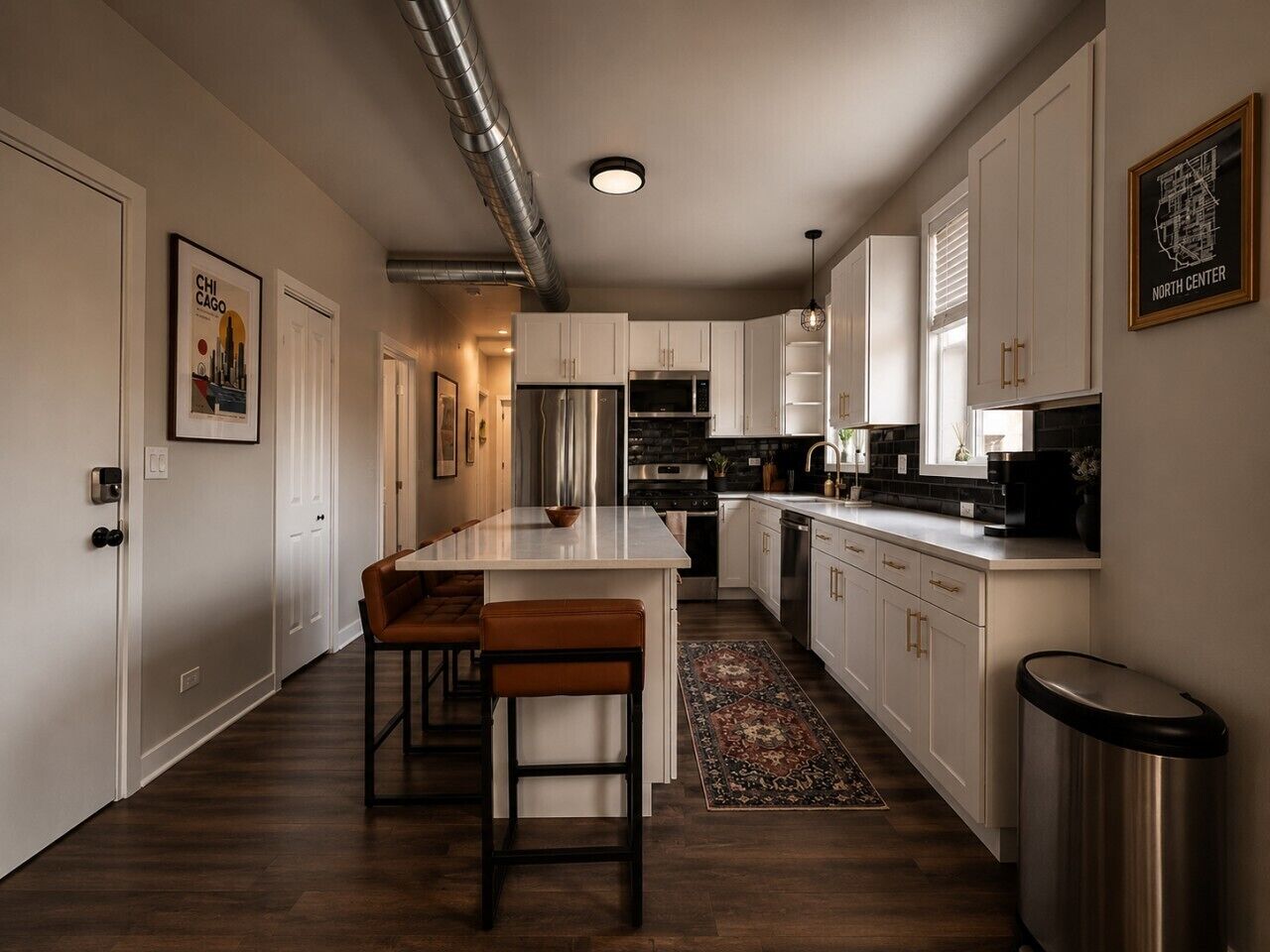 Cocina moderna con una isla central, muebles blancos, electrodomésticos de acero inoxidable y un bote de basura visible.