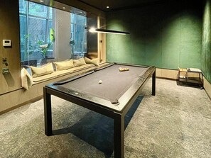 A pool table with a green wall and a sofa in a room with a window. - 2 Bed, 2 Bath-Apartment. West Side Place - Central (Melbourne)