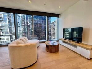 Ein modernes Wohnzimmer mit großem Fenster, einer Couch, einem Couchtisch und einem Flachbildfernseher.