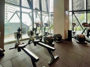 A gym with various exercise equipment, large windows, and a view of buildings outside. - 2 Bed, 2 Bath-Apartment. West Side Place - Central (Melbourne)