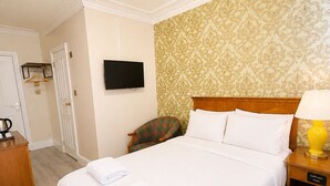 Una habitación de hotel con cama, televisor, mesita de noche con lámpara y armario.