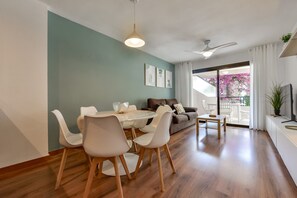 A modern living room with a dining area, a sofa, a TV, and a balcony with pink flowers. - Paraiso Mar Apartments in Calpe VICTORIA (Calpe / Calp)