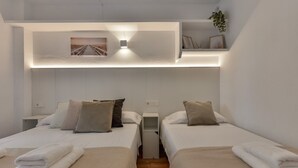 A hotel room with two beds, each with a white bedspread and multiple pillows. There is a small shelf with decorative items and a framed picture above the beds. - Paraiso Mar Apartments in Calpe VICTORIA (Calpe / Calp)