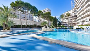 A swimming pool area with multiple pools, palm trees, and a building with balconies in the background. - Paraiso Mar Apartments in Calpe VICTORIA (Calpe / Calp)