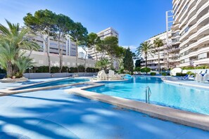 A swimming pool area with multiple pools, palm trees, and a building with balconies in the background. - Paraiso Mar Apartments in Calpe VICTORIA (Calpe / Calp)
