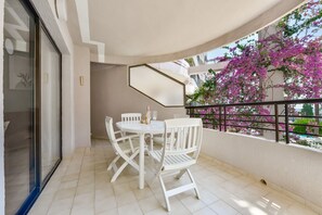 A balcony with a white table and chairs, a glass door, and a view of pink flowers. - Paraiso Mar Apartments in Calpe VICTORIA (Calpe / Calp)
