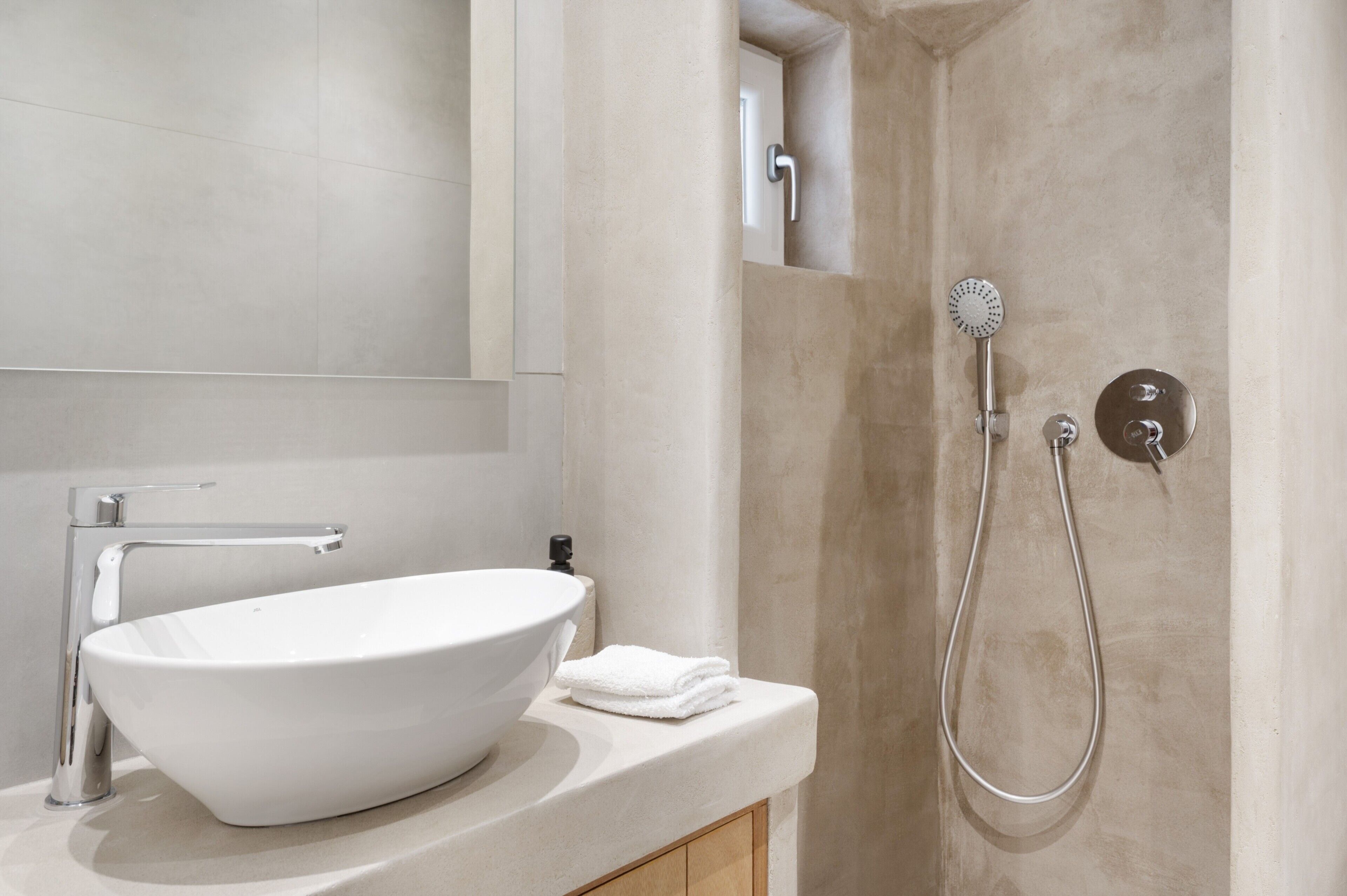 A bathroom with a white sink, a mirror, and a shower with a handheld showerhead.