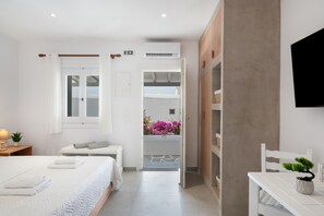 Une chambre d’hôtel avec un lit, une table de chevet avec une lampe, une petite plante en pot et une vue sur un balcon fleuri.